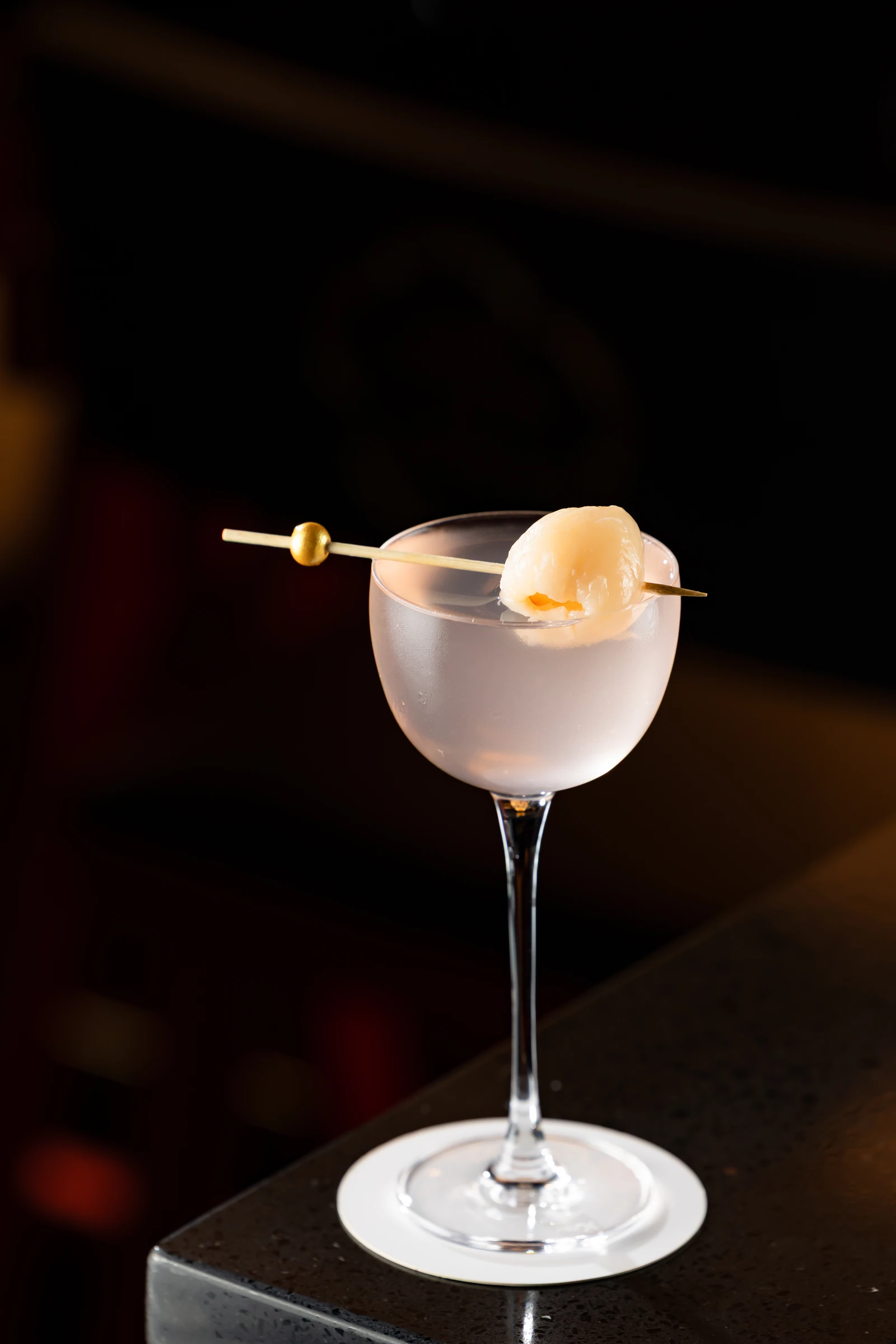 Pale cocktail in a stemmed coupe with a lychee garnish