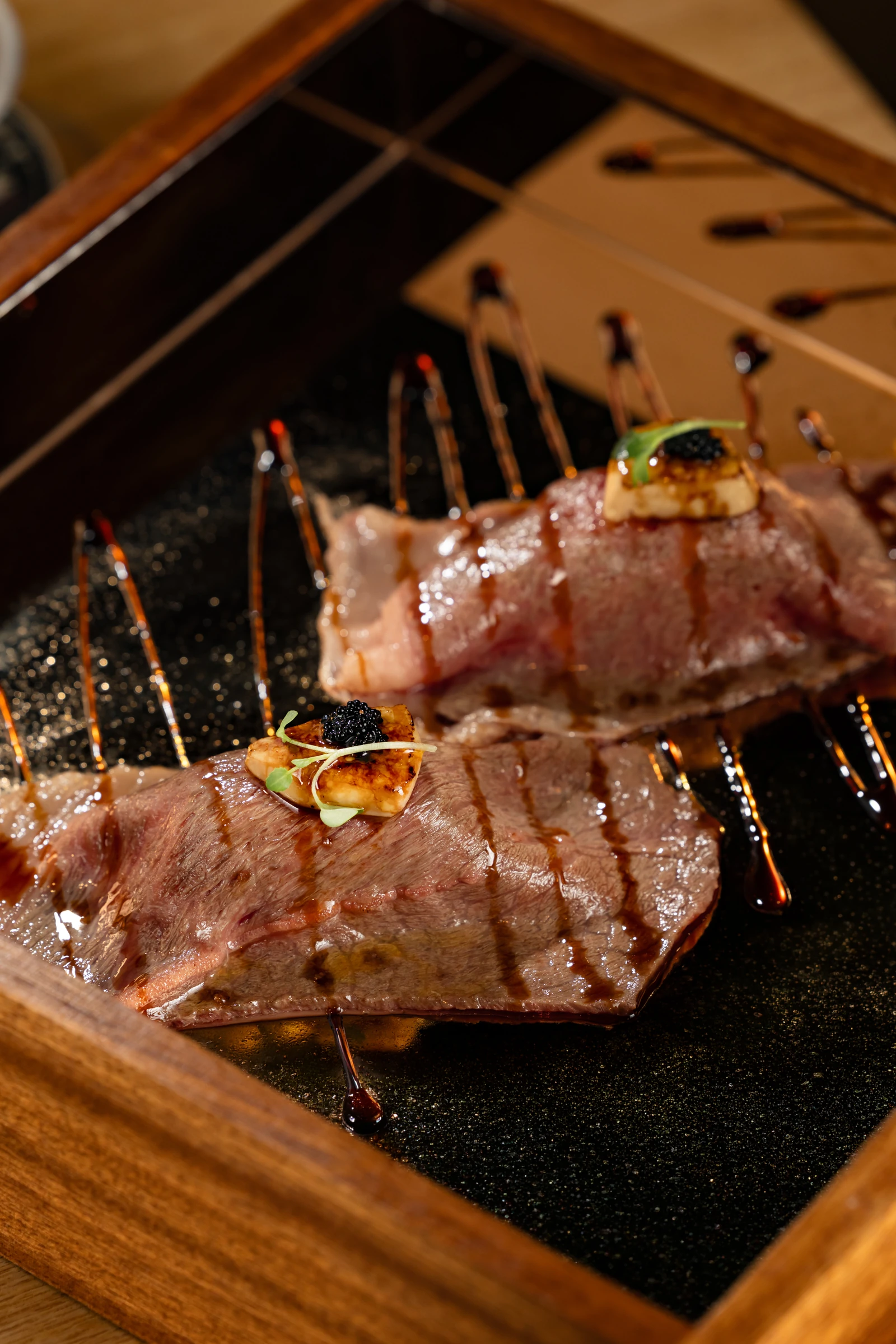 Close view of two seared Wagyu pieces with small garnishes and sauce