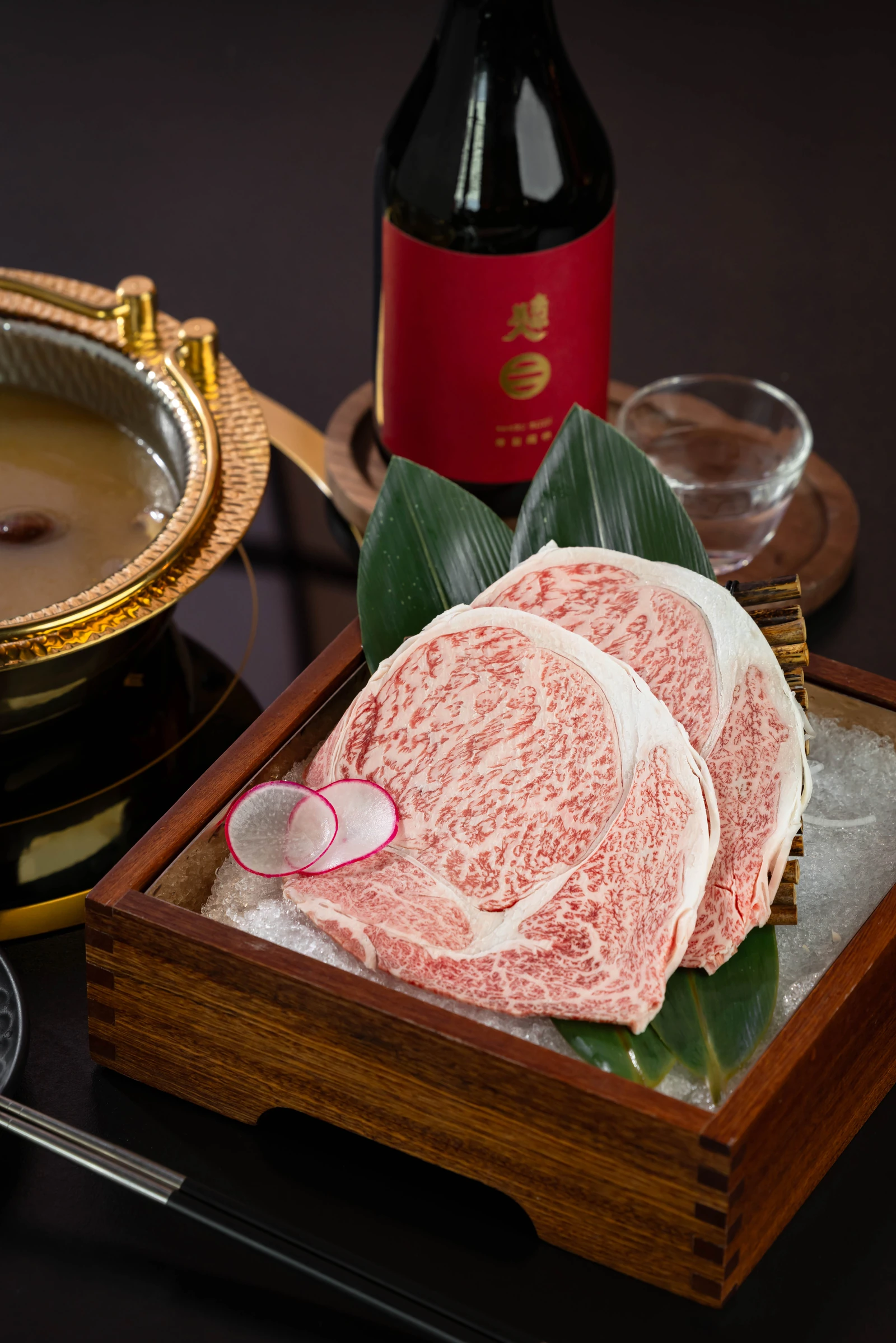 Marbled Wagyu slices presented in a wooden box beside hotpot