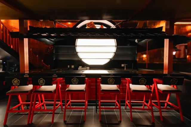 Counter seats with red stools beneath a glowing round window