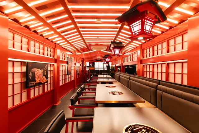 A row of dining tables beneath red beams and hanging lanterns